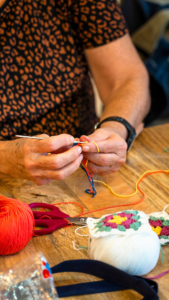 Haakcafe met een tafel met bollen wol in verschillende kleuren. aan tafel zitten een vrouw met een haaknaald het begin van een knuffel te maken