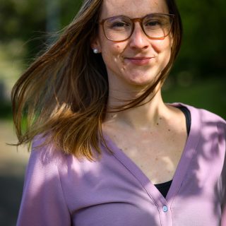 Gerontoloog Charlotte Brys kijkt recht de camera en lacht vriendelijk. Ze draagt een bril en heeft schouderlang en lichtbruin haar.